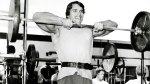 Arnold Schwarzeneggar working out doing an upright barbell row exercise